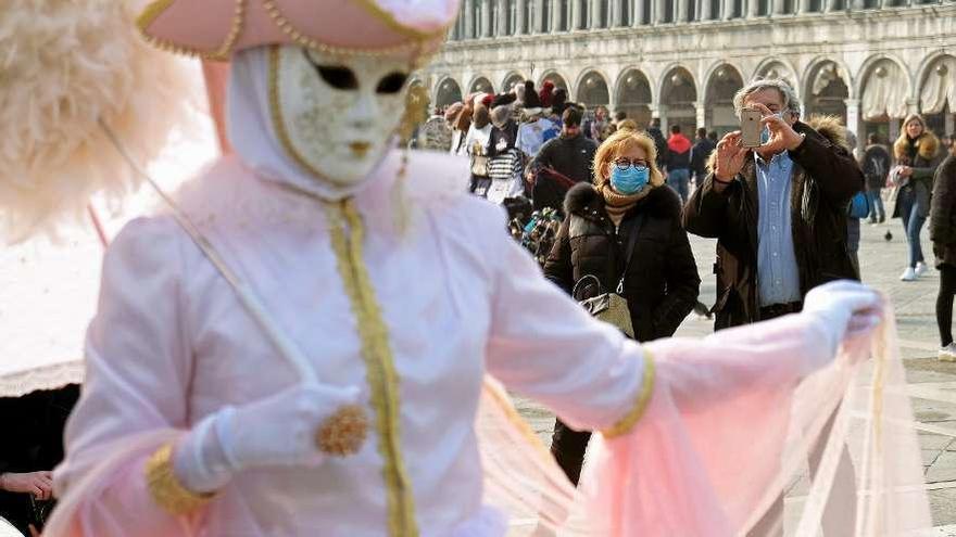 Dos turistas con mascarillas fotografían a una mujer en la plaza de San Marcos de Venecia. // Manuel Silvestri