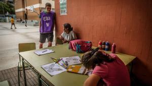 Dos niñas realizan manualidades, ante la mirada de un educador, en la escuela Pau Casals de l’Hospitalet, cuyo patio permanece abierto todo el verano patra actividades de ocio gratuitas.