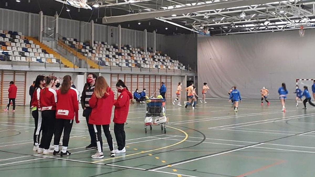 Las jugadoras del Balonmano Gijón, ayer en un corro en La Tejerona, con las del Oviedo Femenino al fondo calentado para disputar un derbi que finalmente no se celebró. | LNE