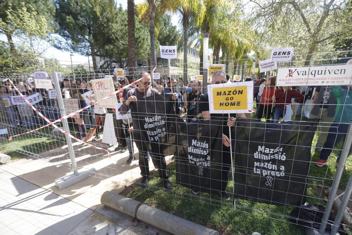 Manifestantes colgando carteles contra Mazón en la valla metálica.