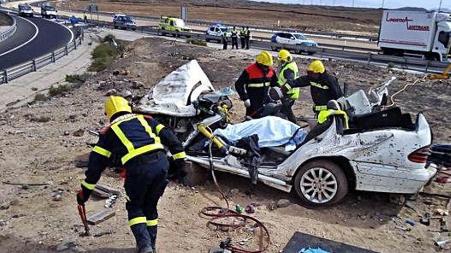 Los Bomberos de La Oliva trabajan junto al coche accidentado, ayer, con el fallecido cubierto con una sábana.