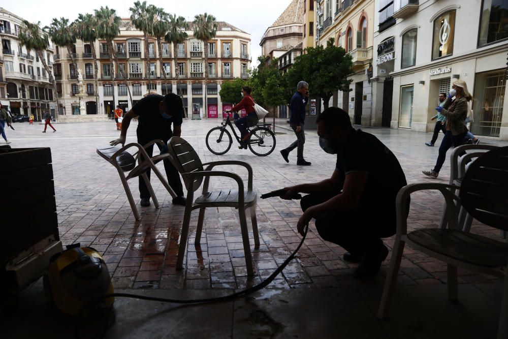 Imágenes de una lluviosa mañana de jueves en el centro de Málaga, donde al paisaje ya habitual de pocas personas y la mayoría de ellas con guantes y mascarillas se le han añadido los preparativos de bares, cafeterías y terrazas que se preparan para el inminente cambio de fase de la desescalada de la ciudad.