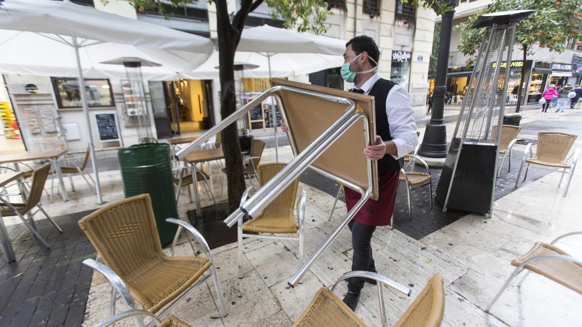 Un camarero recoge la terraza de un bar de València el día previo al cierre total del sector.