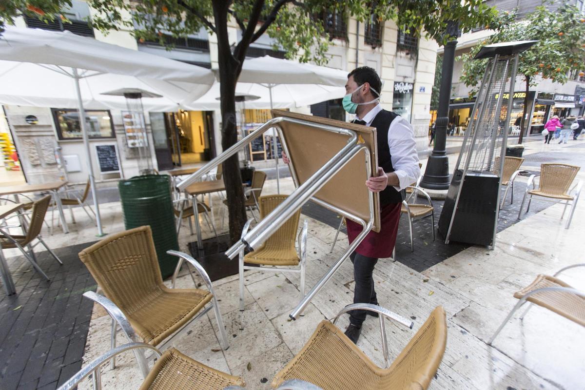 Un camarero recoge la terraza de un bar de València el día previo al cierre total del sector.