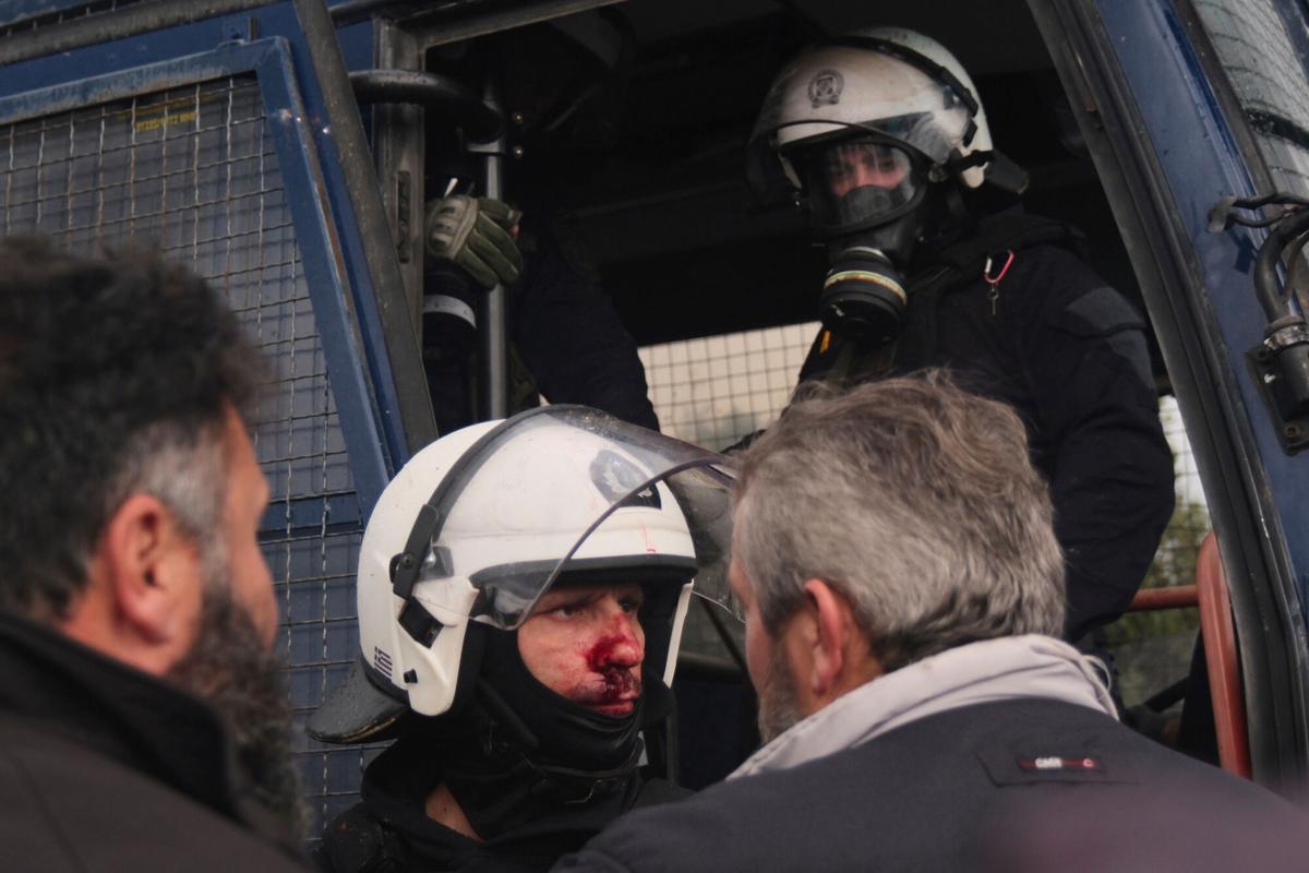A injured police officer stands next to a police bus during clashes with officers blocking their march to Chanias airport on Crete, Greece, Monday, Dec. 8, 2025, amid protests over delayed EU farm subsidies. (AP Photo/Giannis Angelakis)