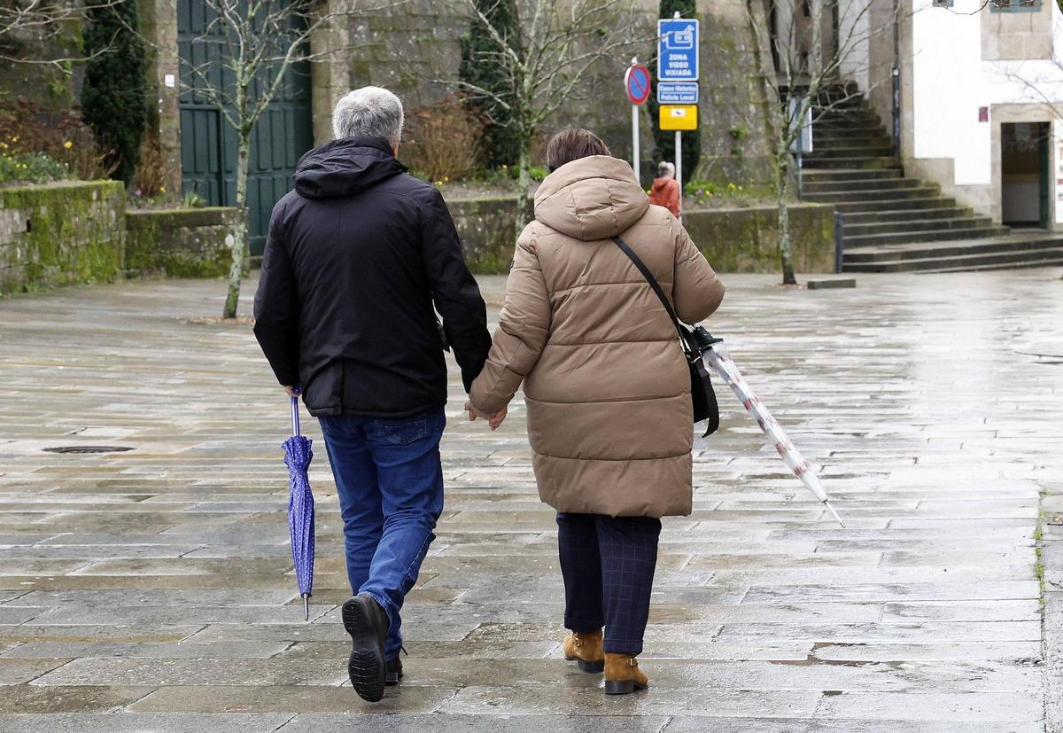 Una pareja pasea de la mano en Santiago ataviados con sus paraguas