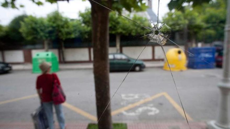 El impacto sobre el cristal, en primer término; a la izquierda, una mujer en la parada del autobús.