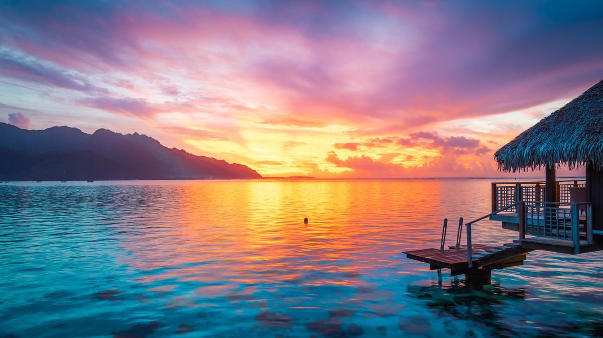 El atardecer en Moorea (Polinesia Francesa) es un espectáculo visual único donde el sol se esconde tras el perfil montañoso de la isla, tiñendo el cielo de intensos naranjas, rosas y violetas que se reflejan en sus tranquilas aguas turquesa.