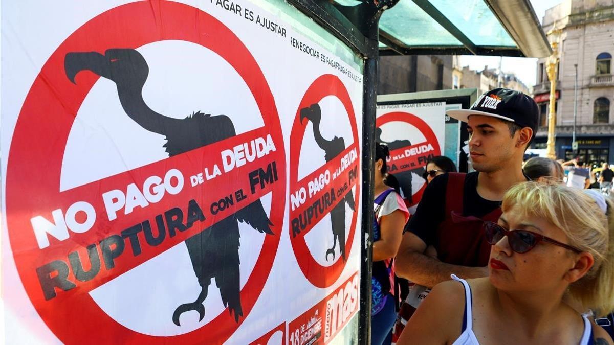 Un grupo de personas pasan junto a un cartel que pide al Gobierno argentino no pagar la deuda al FMI, en Buenos Aires.