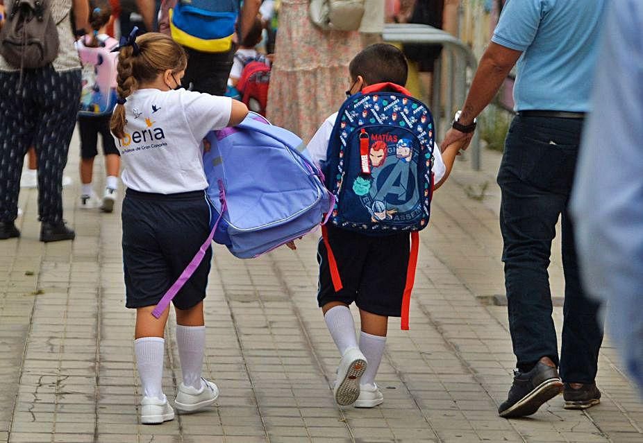 Dos pequeños hacen lo que pueden para llevar sus mochilas. 