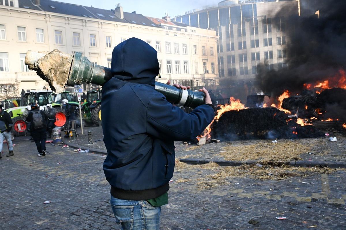 Un agricultor carga con un bolardo durante las protestas en Bruselas contra el acuerdo con Mercosur. El sector rechaza el tratado, que busca integrar un mercado de 780 millones de consumidores, por el impacto que la apertura agrícola tendría sobre los productores europeos. 18 de diciembre de 2025, Bruselas.