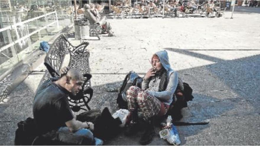Varias personas comiendo en el suelo en la plaza 25 de Mayo frente a las terrazas de los bares llenas de gente.  RAFA ARJONES
