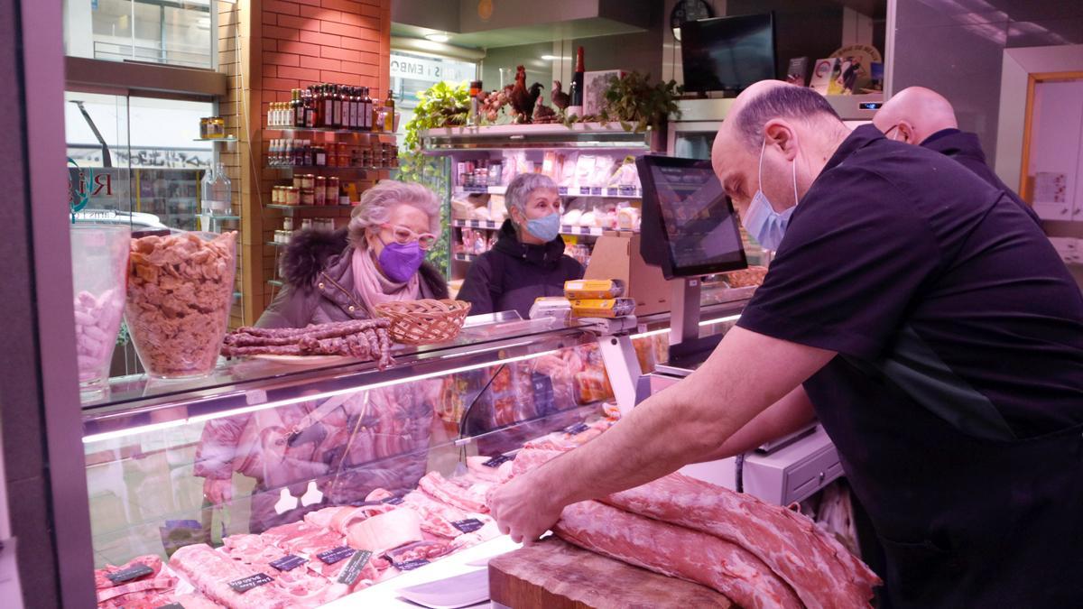 Una clienta espera que el carnisser li talli la peça de carn en una xarcuteria de Girona