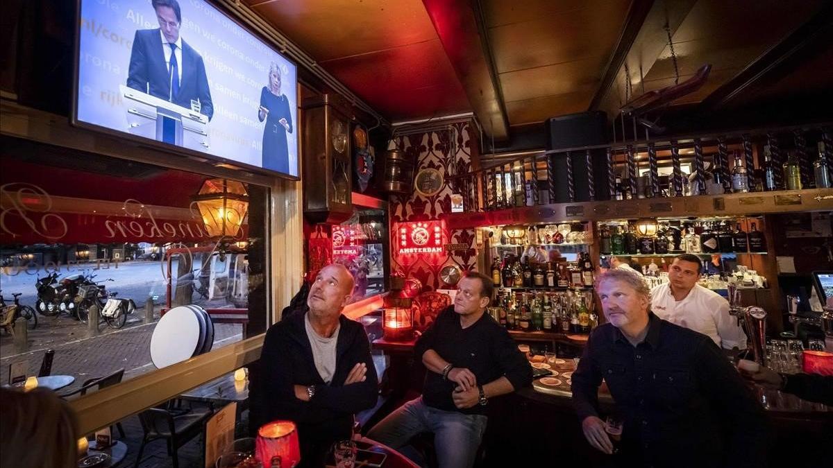 Empleados del café Marcella, en Amsterdam, siguen el mensaje televisado del primer ministro holandés sobre las nuevas restricciones que afectarán a la hostelería.