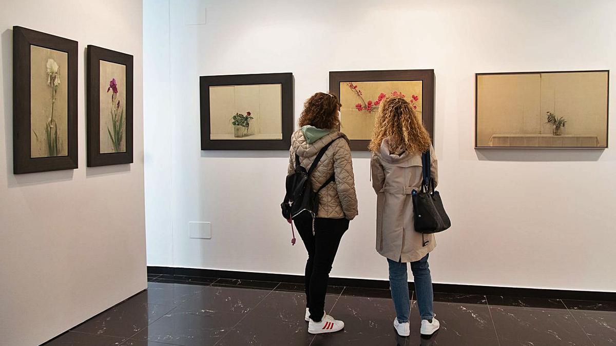 Dos visitantes observan algunos de los cuadros con motivos florales en la galería Espacio 36.