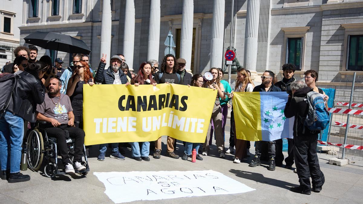 Varias personas protestan contra el modelo turístico en Canarias frente al Congreso de los Diputados.
