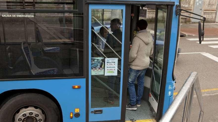 Viajeros subiendo al autobús en Pola de Laviana, con las nuevas tarifas marcadas en la puerta.