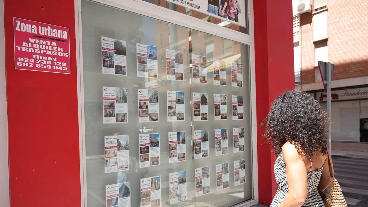Una joven mira los anuncios de pisos en alquiler en la fachada de una inmobiliaria de Badajoz.
