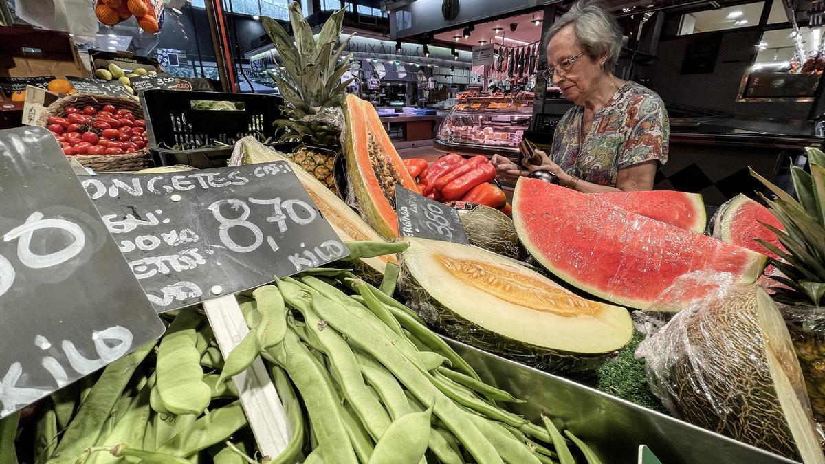 Una mujer observa los productos de una frutería en un mercado.