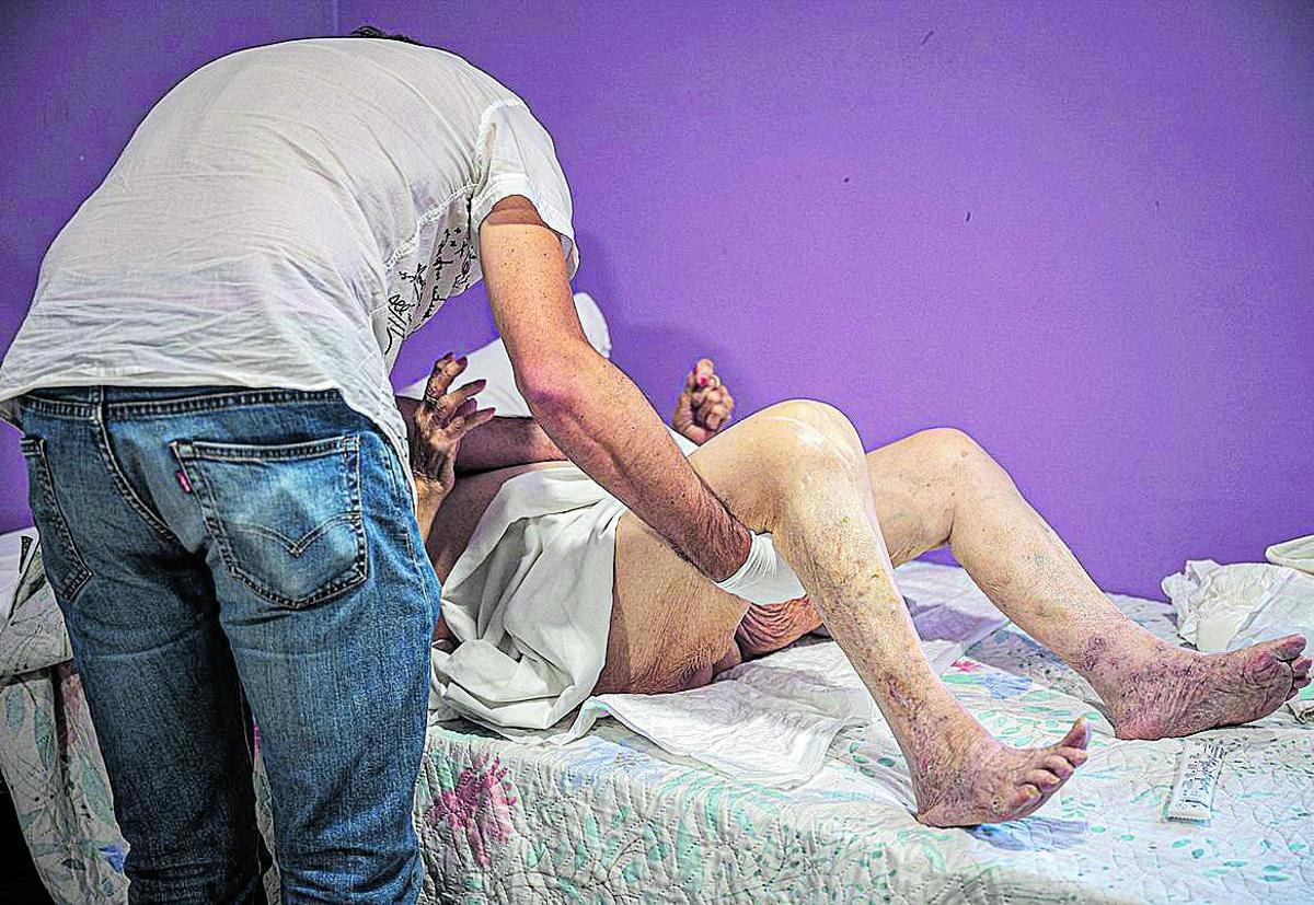 En el geriátrico, el mé́dico intenta colocar a una residente en la postura adecuada para una exploración ginecológica.