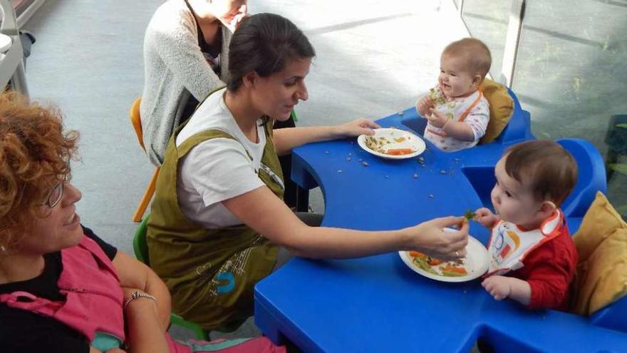 Una trabajadora del centro en el comedor con dos bebés.