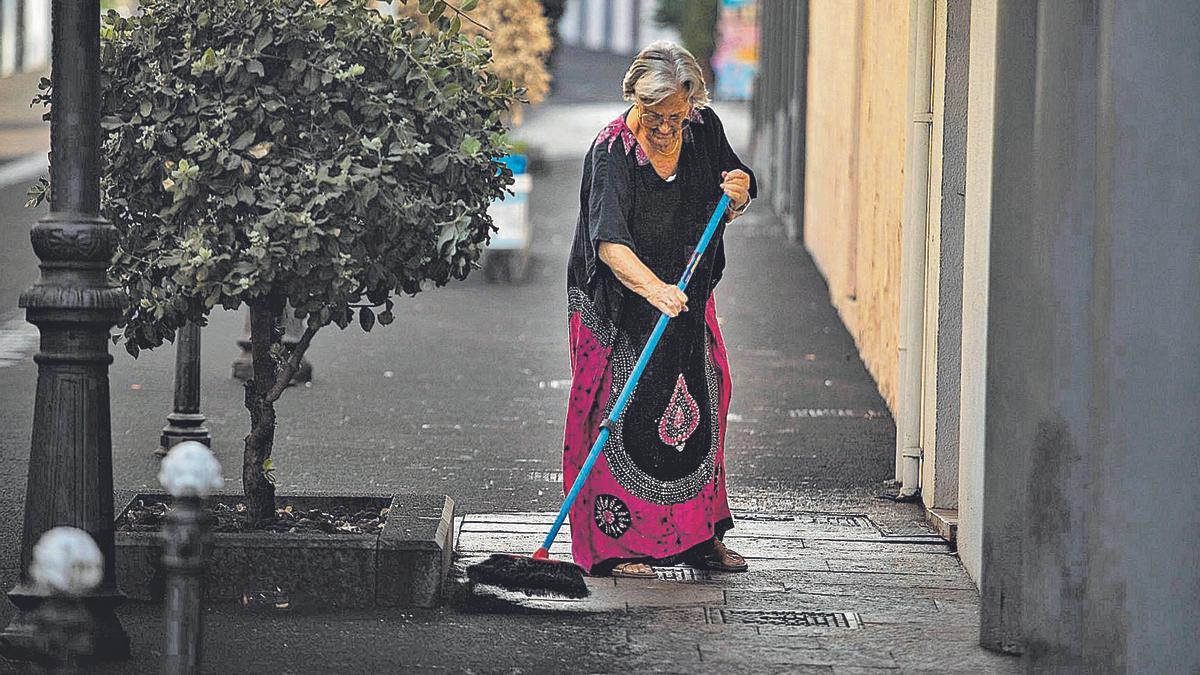 Una vecina de Los Llanos de Aridane barre la ceniza ante la puerta de su casa.  | | 