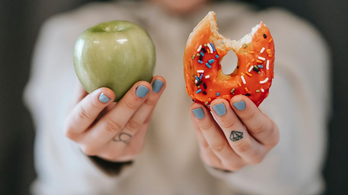 Una persona sujeta una manzana y una rosquilla