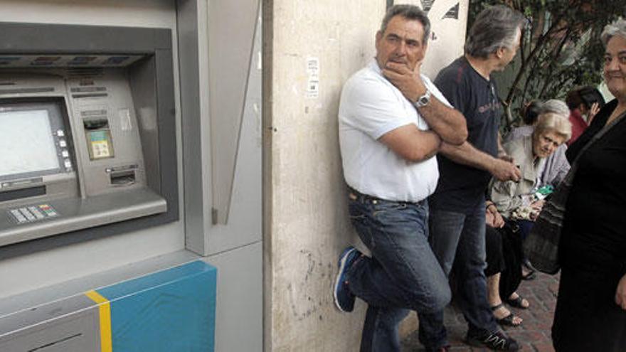 Varias personas esperan junto a un cajero que no funciona en Grecia.