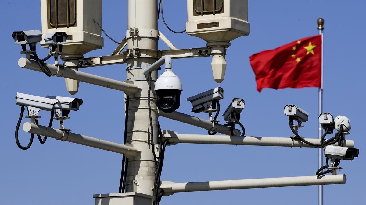 Una bandera nacional china ondea cerca de las cámaras de vigilancia montadas en un poste de luz en la Plaza Tiananmen. El Primer Ministro chino Li Keqiang negó  que Pekín ordene a sus compañías espiar en el extranjero. 