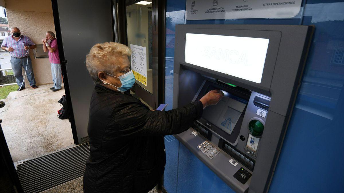 Una mujer mayor utilizando un cajero automático en una sucursal del interior de la provincia de Pontevedra.