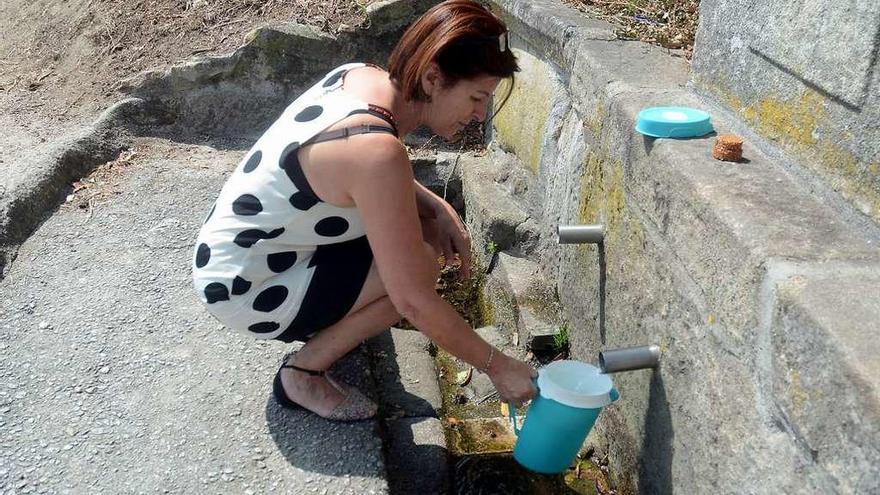 Una mujer trata de recoger agua en Poio de una fuente con escaso caudal por la sequía. // Rafa Vázquez