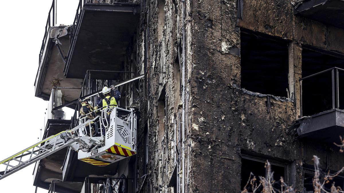 Bomberos en una grúa sanean la fachada quemada en el edificio de Valencia.