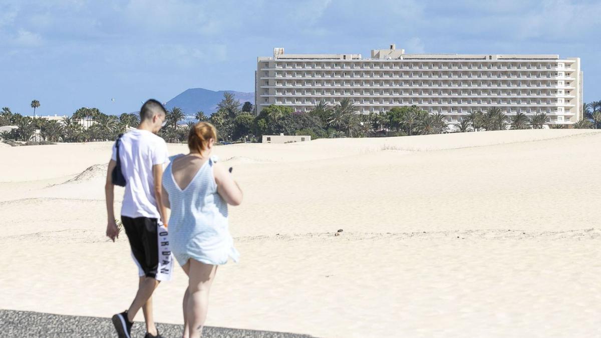 Una pareja camina por el complejo dunar de Corralejo con el hotel Oliva Beach al fondo. | | LP/DLP