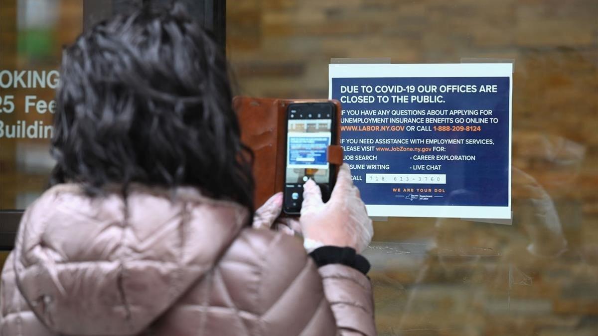 Una mujer toma una foto de un cartel colgado frente a una oficina del Departamento de Trabajo cerrada por coronavirus, este miércoles en Nueva York.