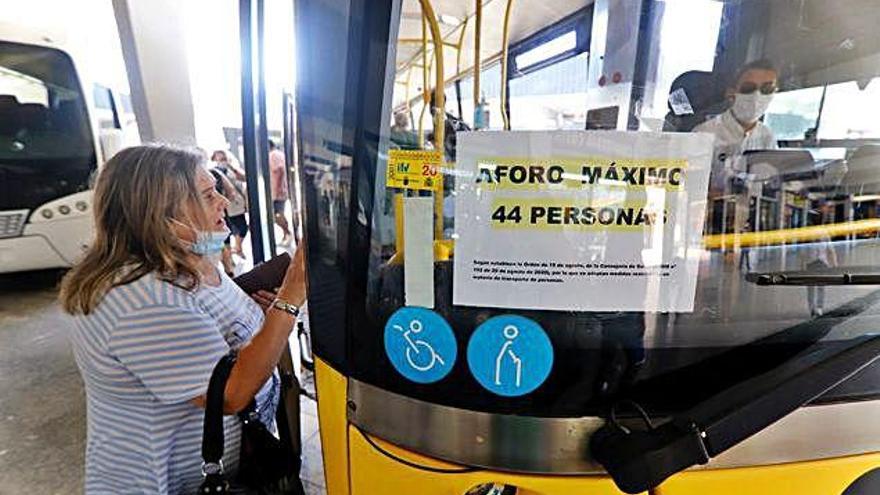 Una mujer consulta el horario al chófer y espera frente a la puerta del autobús para evitar quedarse sin asiento.