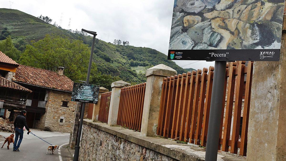 Un vecino pasa con sus perros junto a las obras de la exposición callejera de César Fernández Pello, “Xastre”, en Bueño. | Luisma Murias