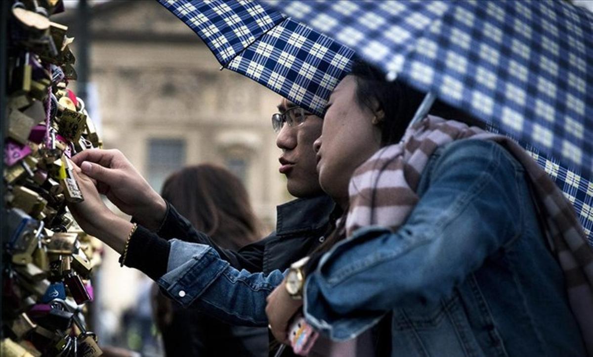 Una parella de turistes xinesos posa un candau al pont de les Arts, de París, el 31 de maig del 2015, un dia abans que les autoritats hagin començat a retirar tots els candaus de l’estructura del pont.