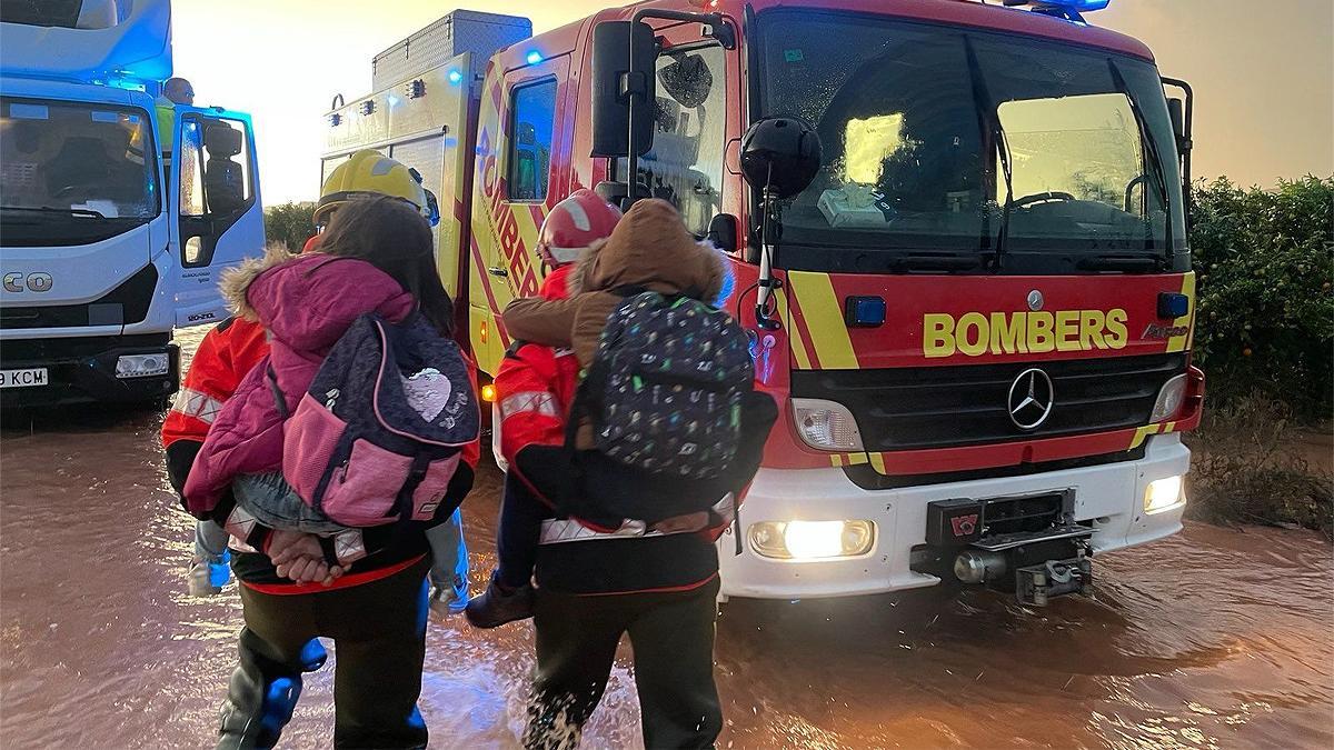 Dos bomberos llevan a dos niños en Castellón, donde han caído fuertes precipitaciones.