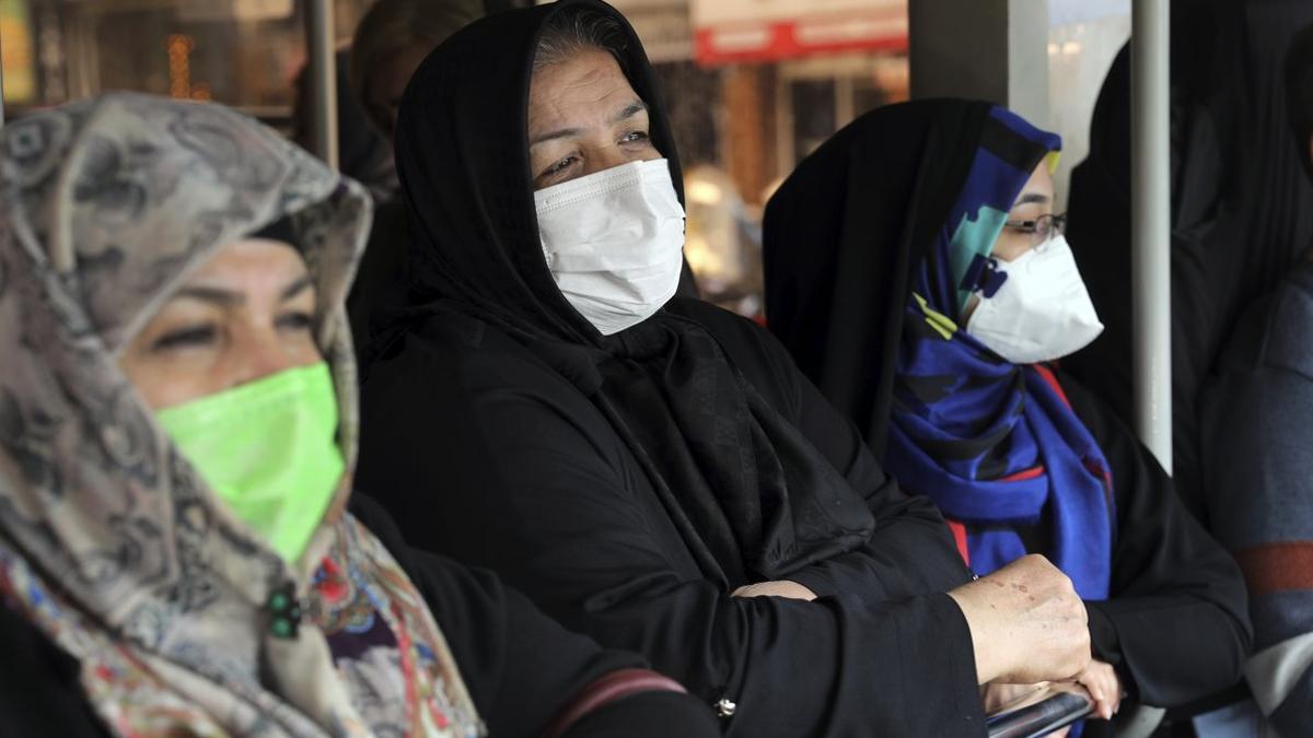 Unas mujeres con mascarilla esperan el autobús, en una parada de Teherán.