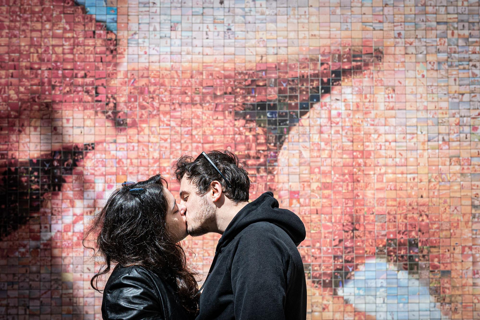 Una pareja de jóvenes se besan frente al mural del beso en Barcelona.