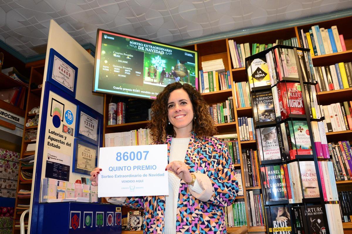 Elena Bangueses muestra el cartel con el número agraciado en la Librería Abrente mientras en la televisión continúa el Sorteo Extraordinario de Navidad.