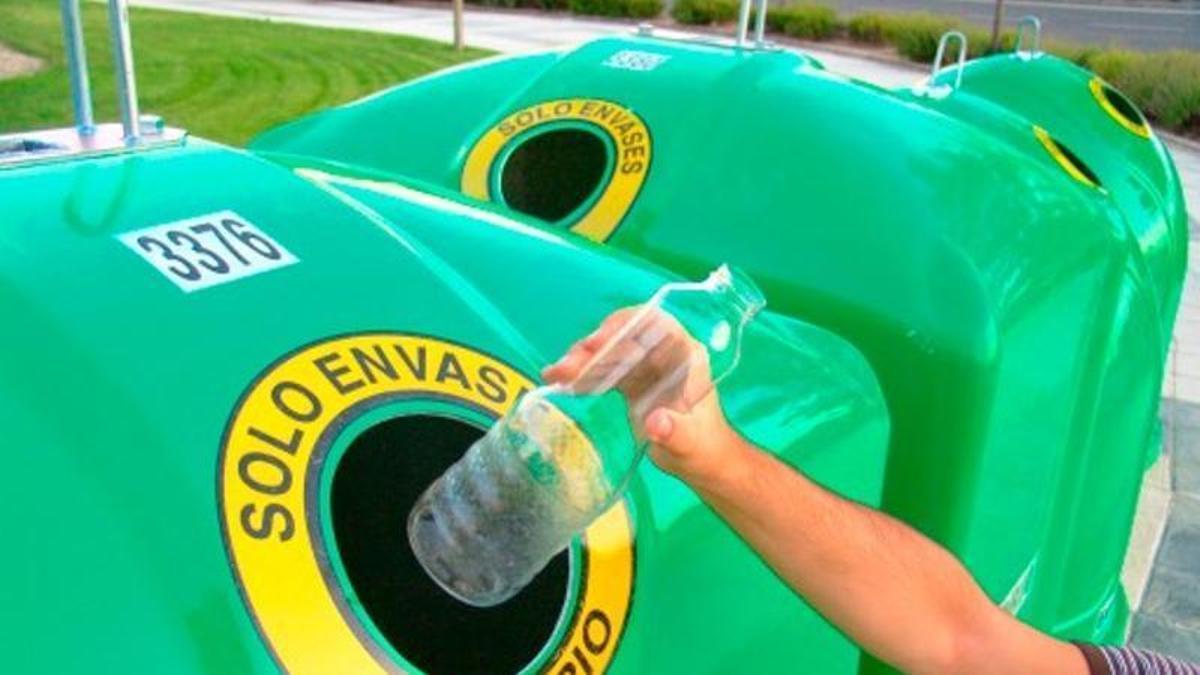 Un consumidor deposita una botella de vidrio en el contenedor verde.