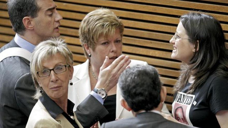 La portavoz del grupo Compromis en Les Corts Valencianes, Mónica Oltra (d), discute con el portavoz popular, Ricardo Costa (i), en presencia de la presidenta de Les Corts Valencianes, Milagrosa Martínez (c), por llevar puesta una camiseta con una fotografía del presidente de la Generalitat, Francisco Camps, y el lema en inglés &quot;Se busca. Sólo vivo&quot;, hecho por el que tuvo que abandonar el pleno.