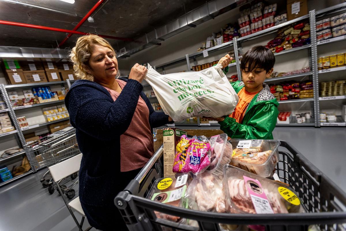 Sonia Idrovo, junto a su hijo, rellenando el carro de la compra en la entidad De Veí a Veí, en el barrio de Sant Antoni.
