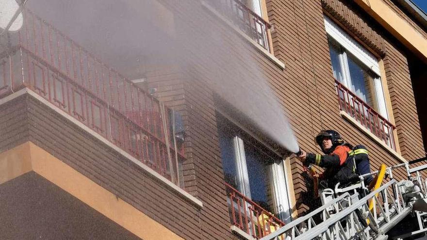 Un bombero trata de sofocar las llamas desde la escala en la calle Churruca.