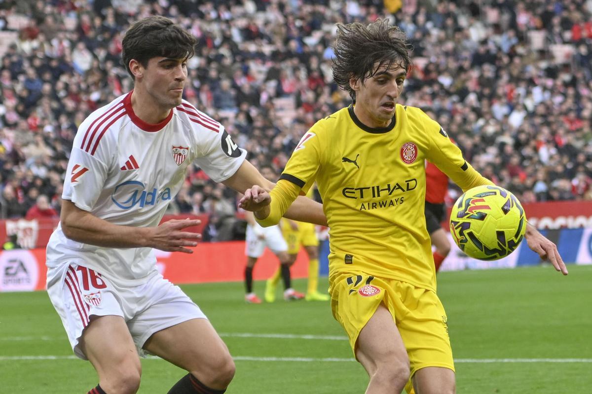 SEVILLA, 08/02/2026.- El jugador del Sevilla Juanlu Sanchez (L) y el delantero del Girona, Bryan Gil Salvatierra (d) luchan por el balón durante el partido de la jornada 23 de Liga que el Sevilla y el Girona disputan este domingo en el estadio Ramón Sánchez Pizjuán de Sevilla. EFE/ Raul Caro