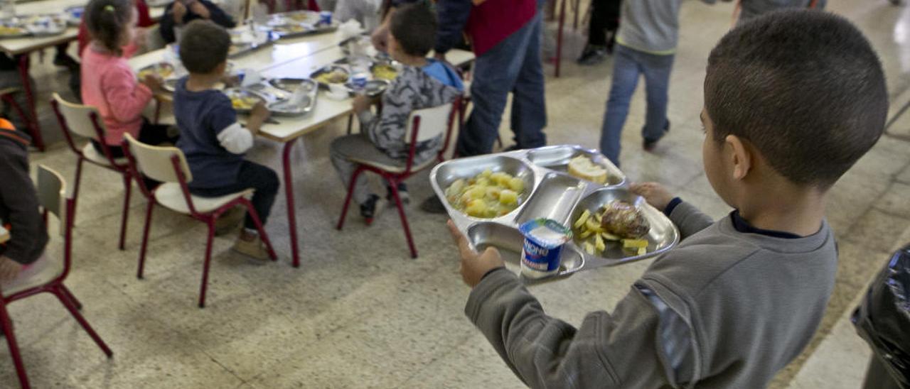Un alumno lleva su bandeja con el menú escolar a la mesa.
