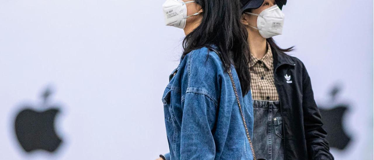 Dos chicas, con sus mascarillas, ante la tienda de Apple de Shenzhen, en China. / Efe