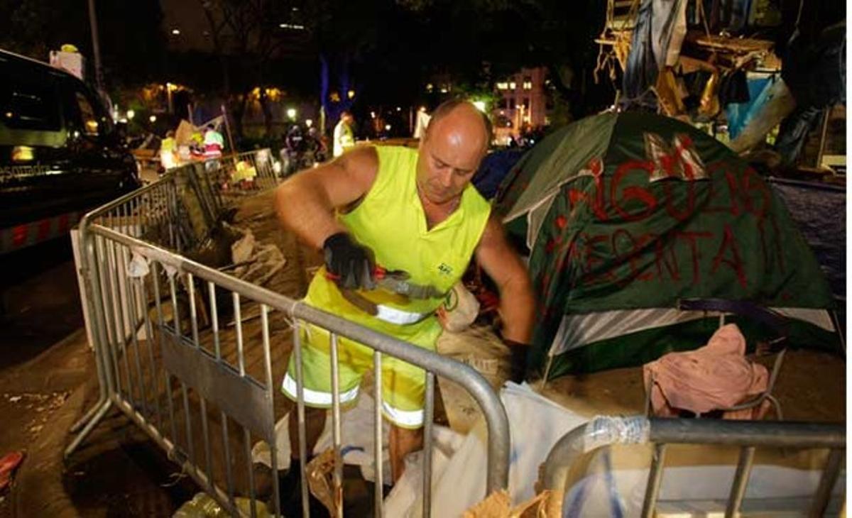 Un membre dels serveis de neteja retira els objectes instal·lats en una de les zones de l’acampada de la plaça de Catalunya.