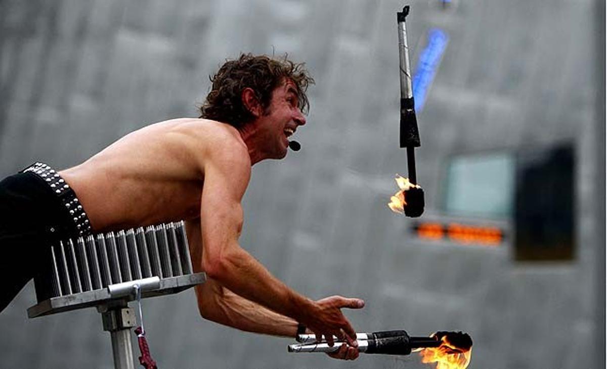 Un artista de carrer fa malabars amb bastons de foc mentre està estirat en un llit de claus, al centre de Melbourne (Austràlia).